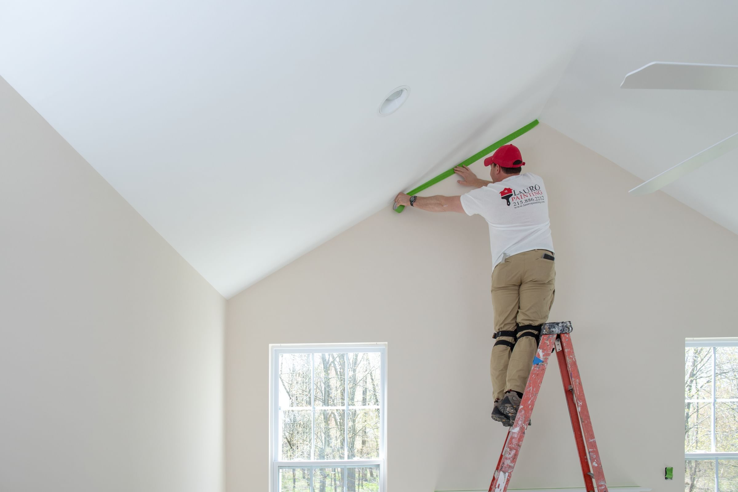 Painter on ladder applying Green FrogTape Multi-Surface Painter's Tape to the seam between the ceiling and wall
