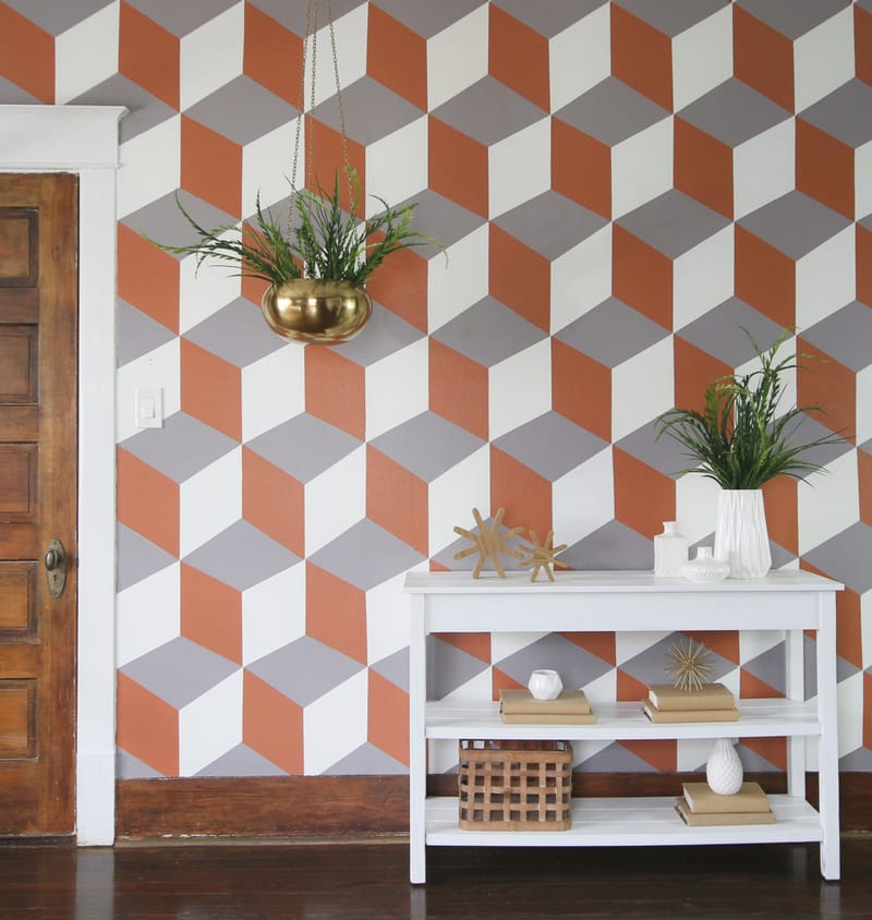 A Geometric cube mural on a wall (Grey, burnt orange, and white), with a small white table in front