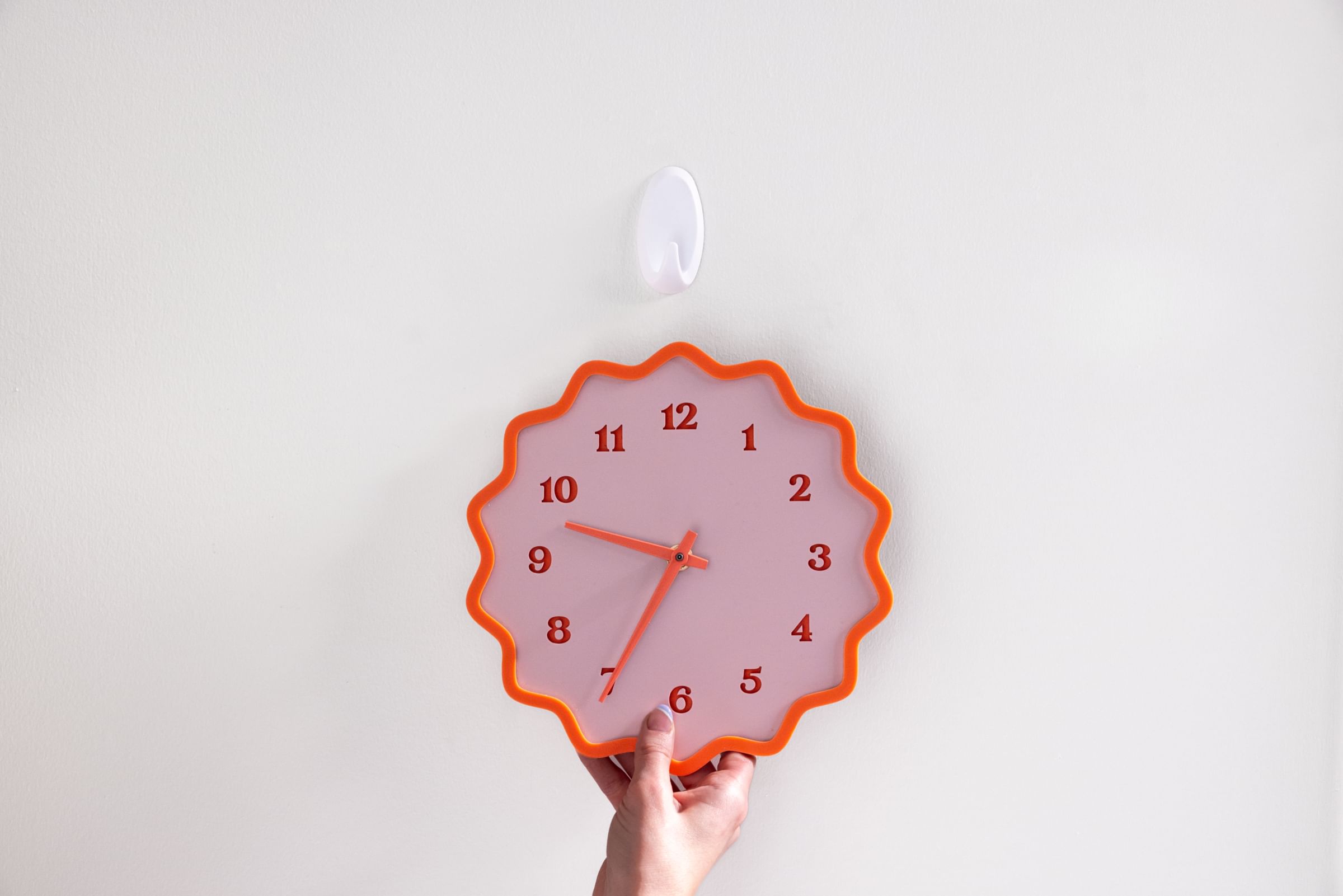 A clock about to be hung on a white FrogTape reMOVEables Hook