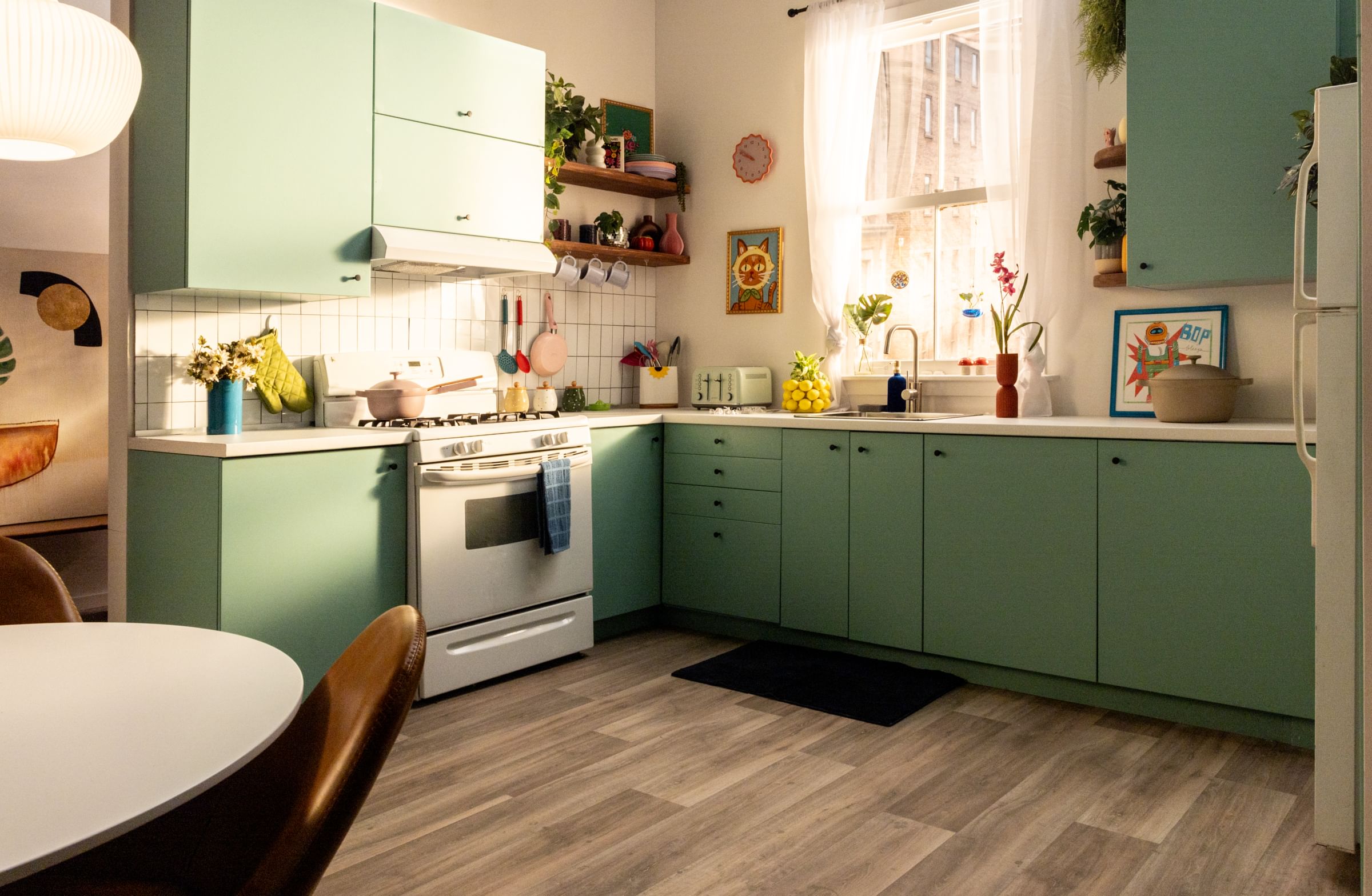 A Kitchen with teal green cabinets and FrogTape reMOVEables used to hang kitchen utensils, a pan, mugs, and more