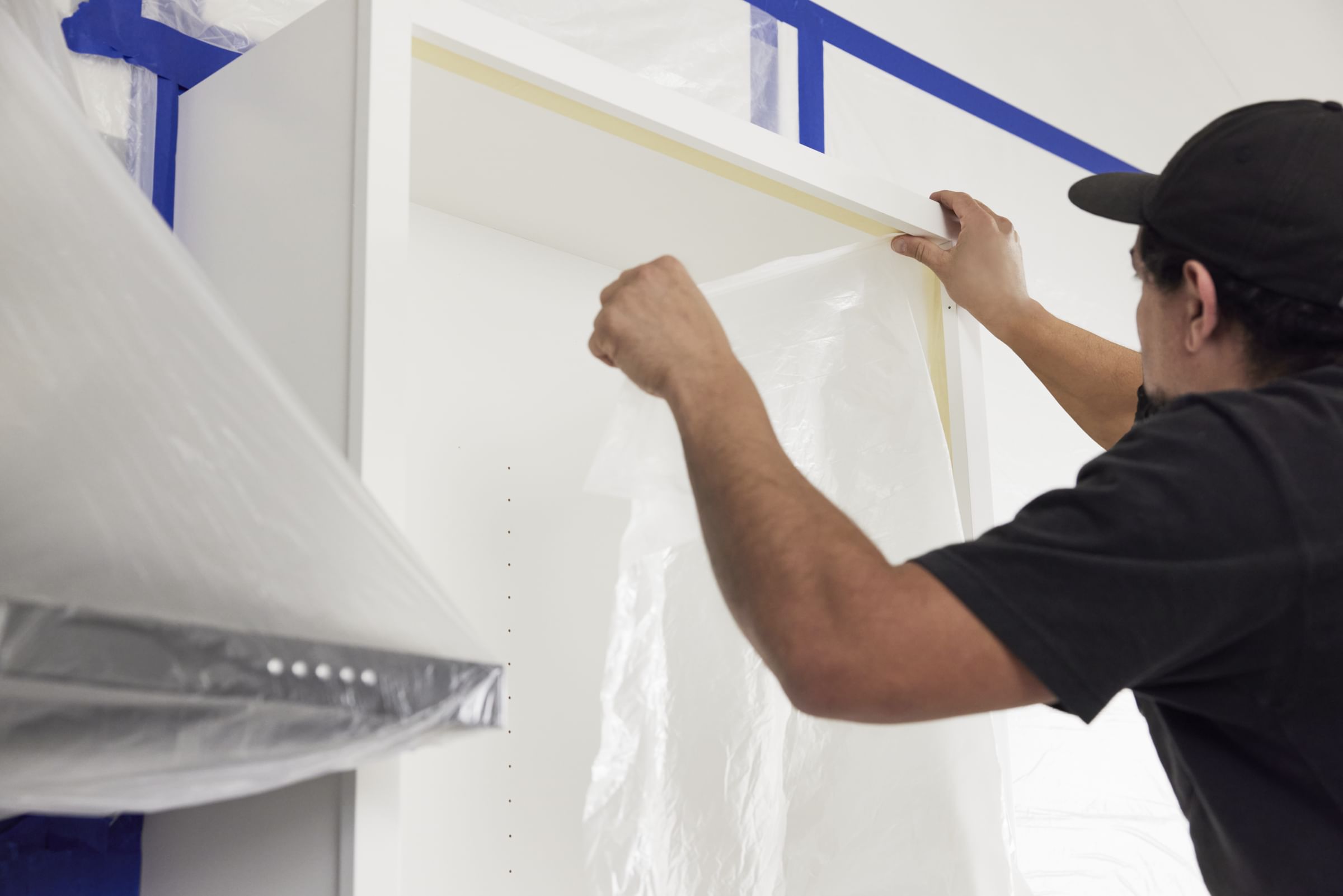 A man using FrogTape DS 154, applying plastic sheeting to a white cabinet.
