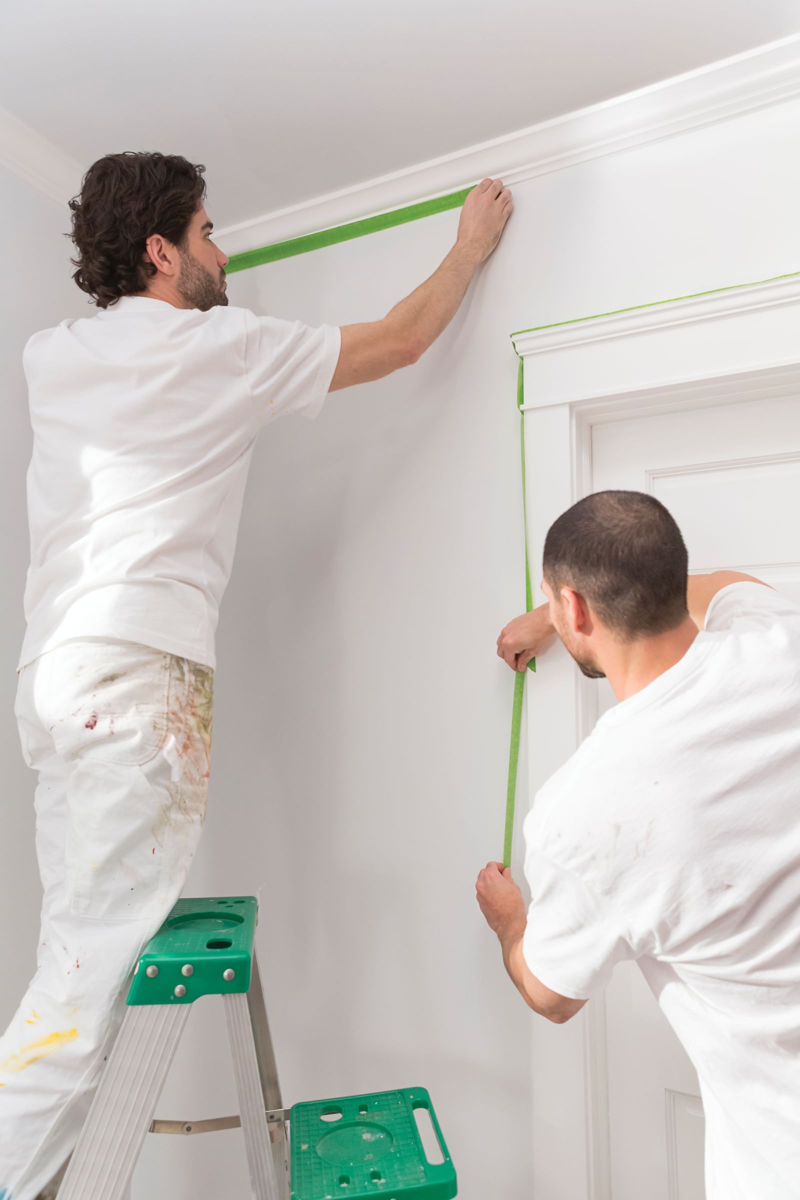Two Paint contractors using Green FrogTape Multi-Surface Painter's Tape to Tape off door and ceiling trim.