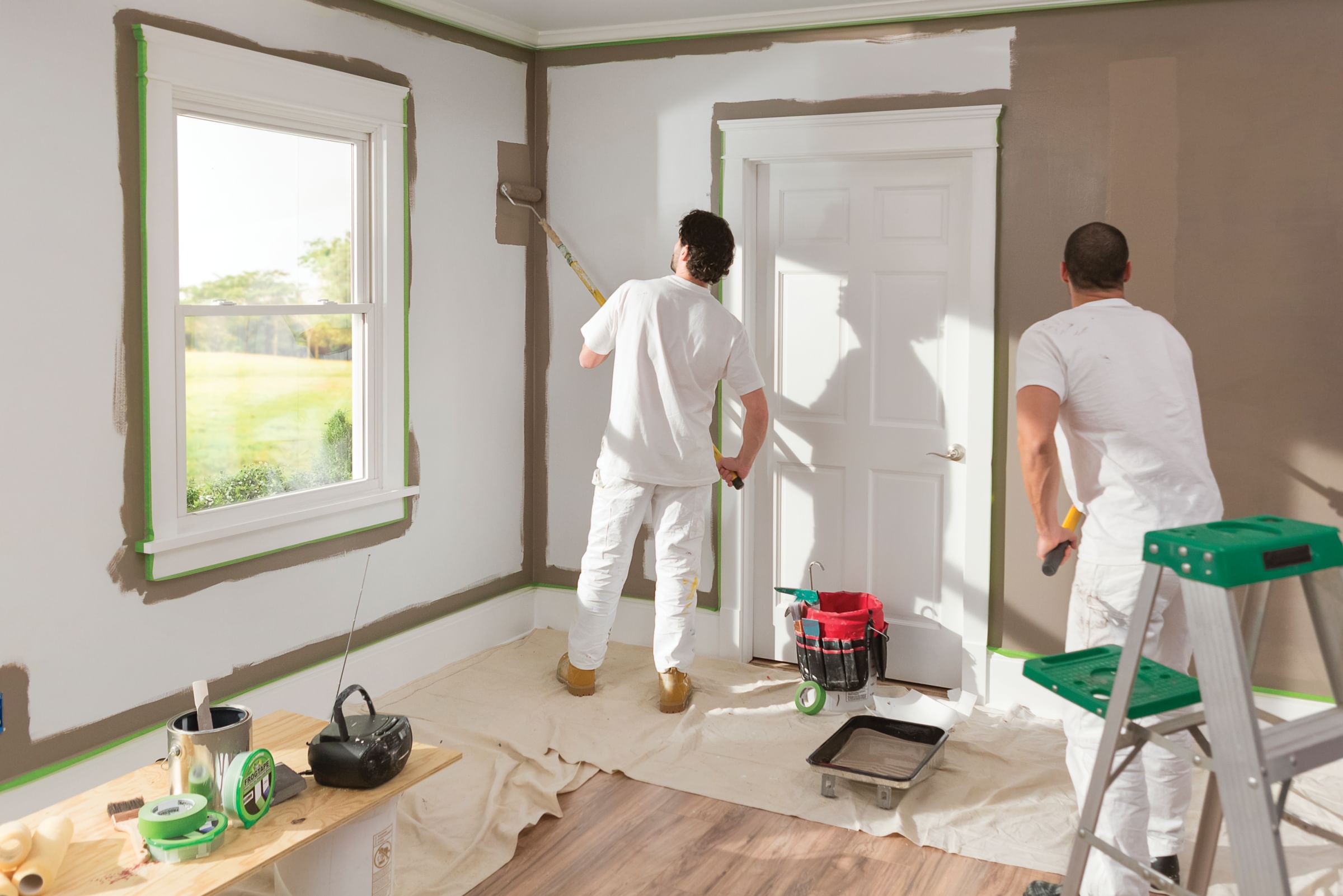 Two painters painting a room brown with paint rollers