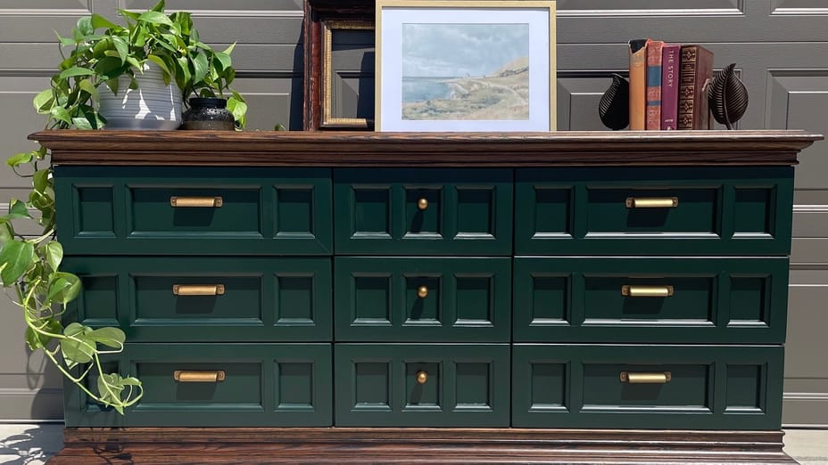 Green Dresser with brown top and bottom and gold handles. There are some books, a couple picture frames, and a plant sitting on the top.