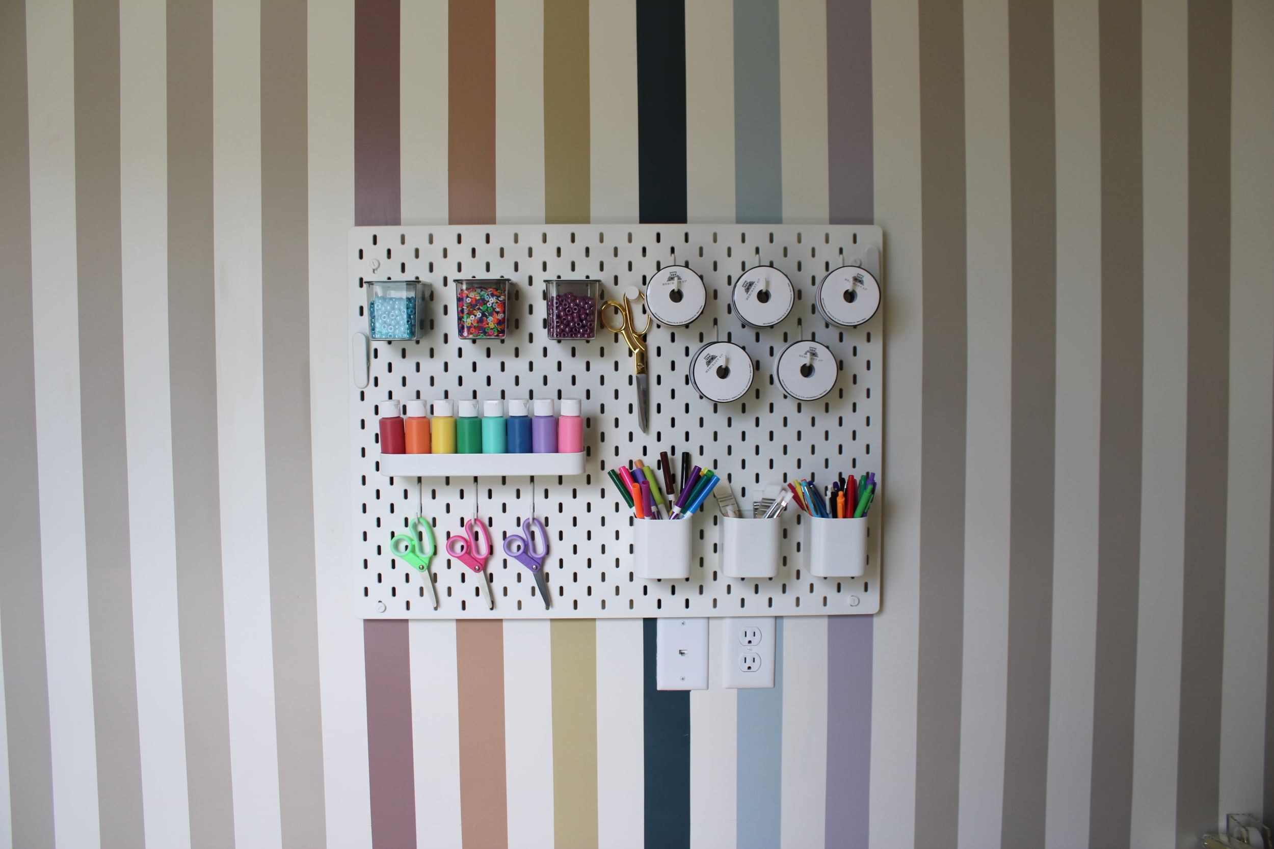 Striped craft wall with white pegboard with craft materials hanging