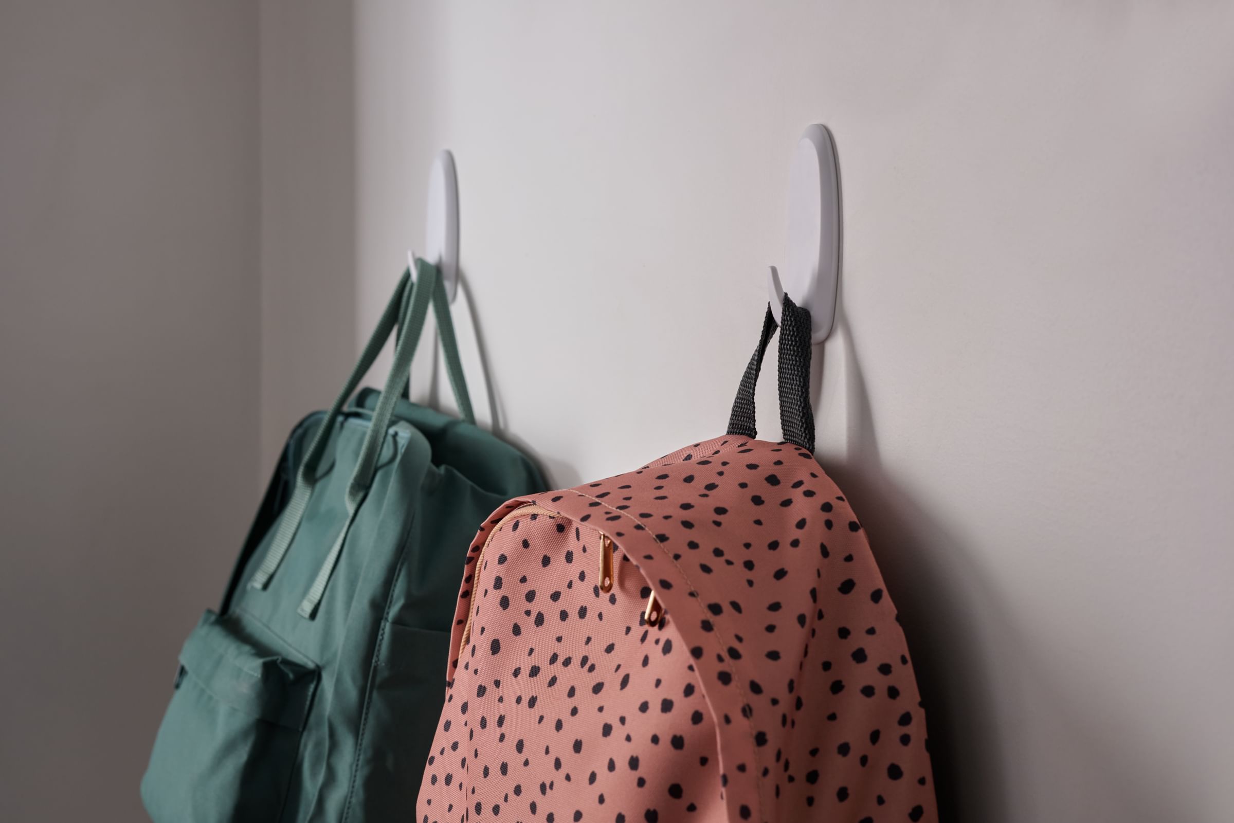 Two white FrogTape reMOVEables Heavy Duty Hooks with backpacks hanging on each