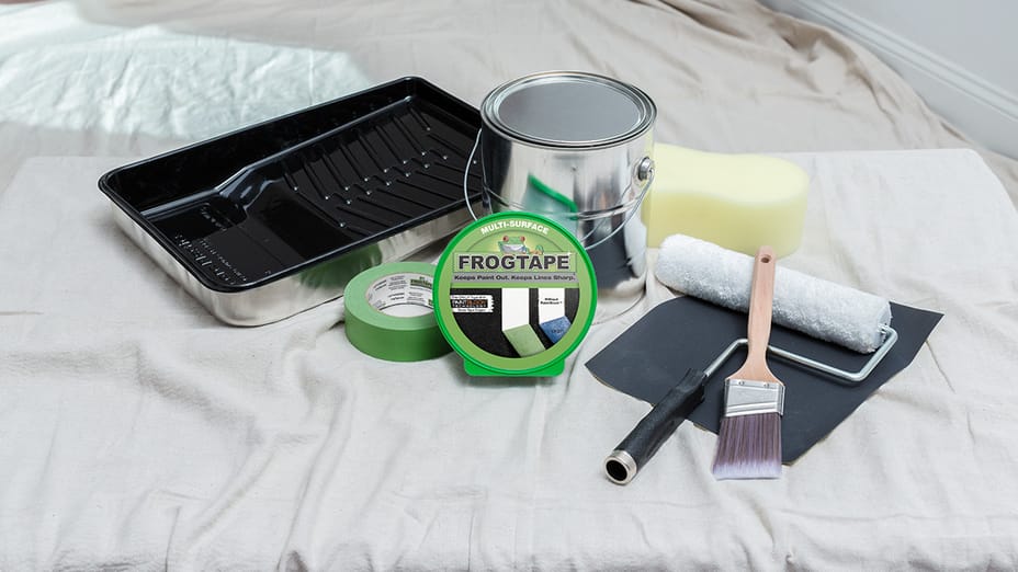 Painting equipment laid out on a drop cloth. Paint tray, Paint Can, FrogTape Multi-Surface Painter's Tape, Sponge, Paint Roller, and Paint Brush