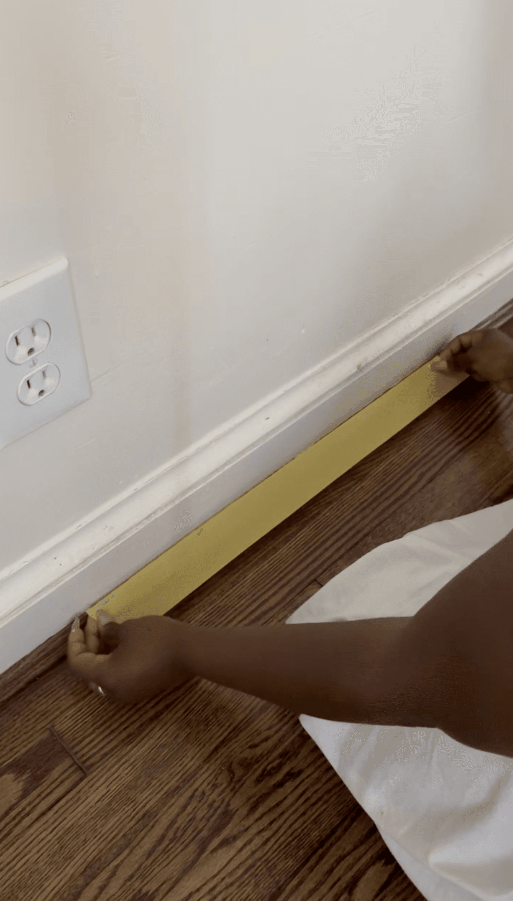 Yellow FrogTape Delicate Surface Painter's Tape being applied to where baseboard trim meets the wood floor