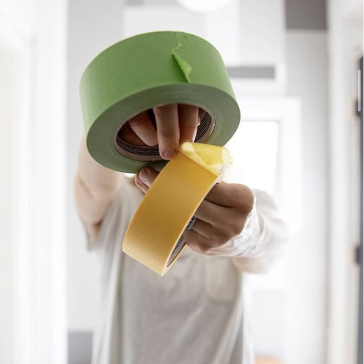 A person holding a roll of Green FrogTape Multi-Surface Painter's Tape and a roll of Yellow FrogTape Delicate Surface Painter's Tape