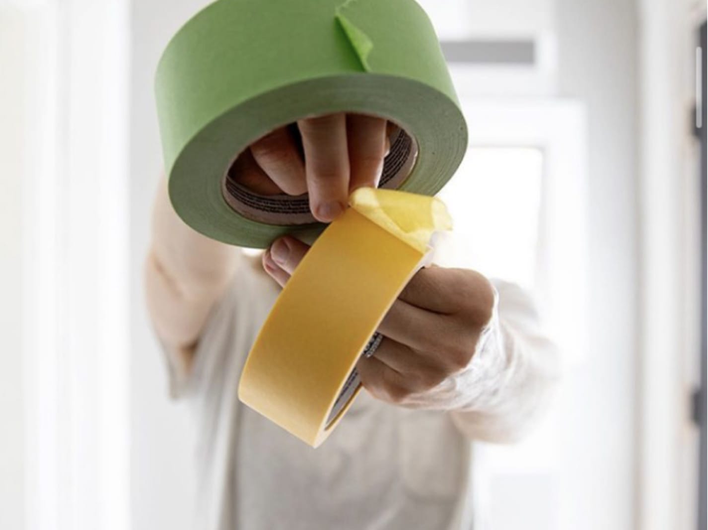 A person holding a roll of Green FrogTape Multi-Surface Painter's Tape and a roll of Yellow FrogTape Delicate Surface Painter's Tape
