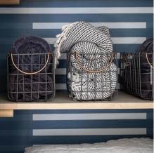 Three metal baskets on a wooden shelf with blankets in them. The back wall is back blue with alternating thin rectangle strips