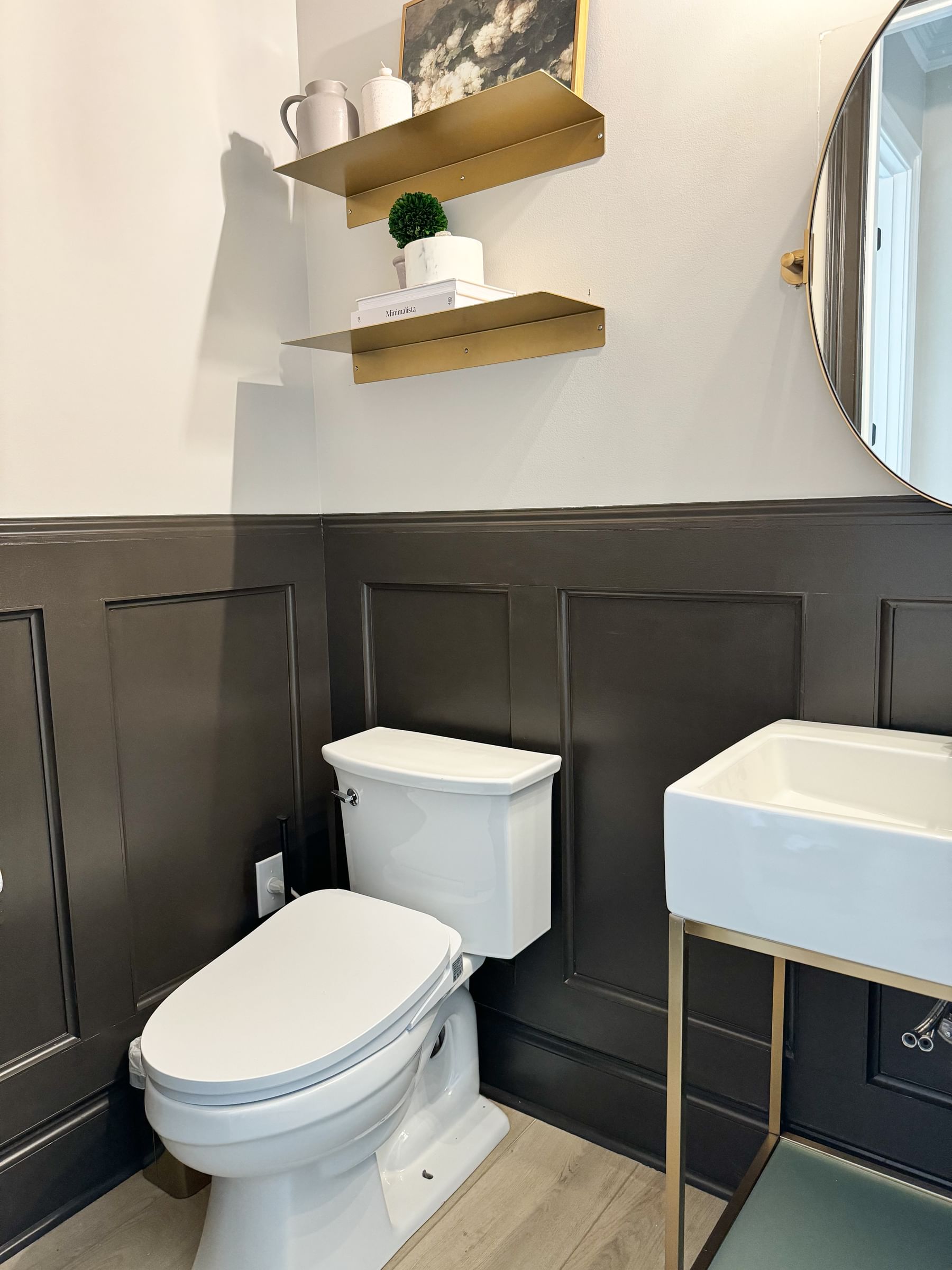 Small half bathroom with updated brown wainscotting and gold floating shelves