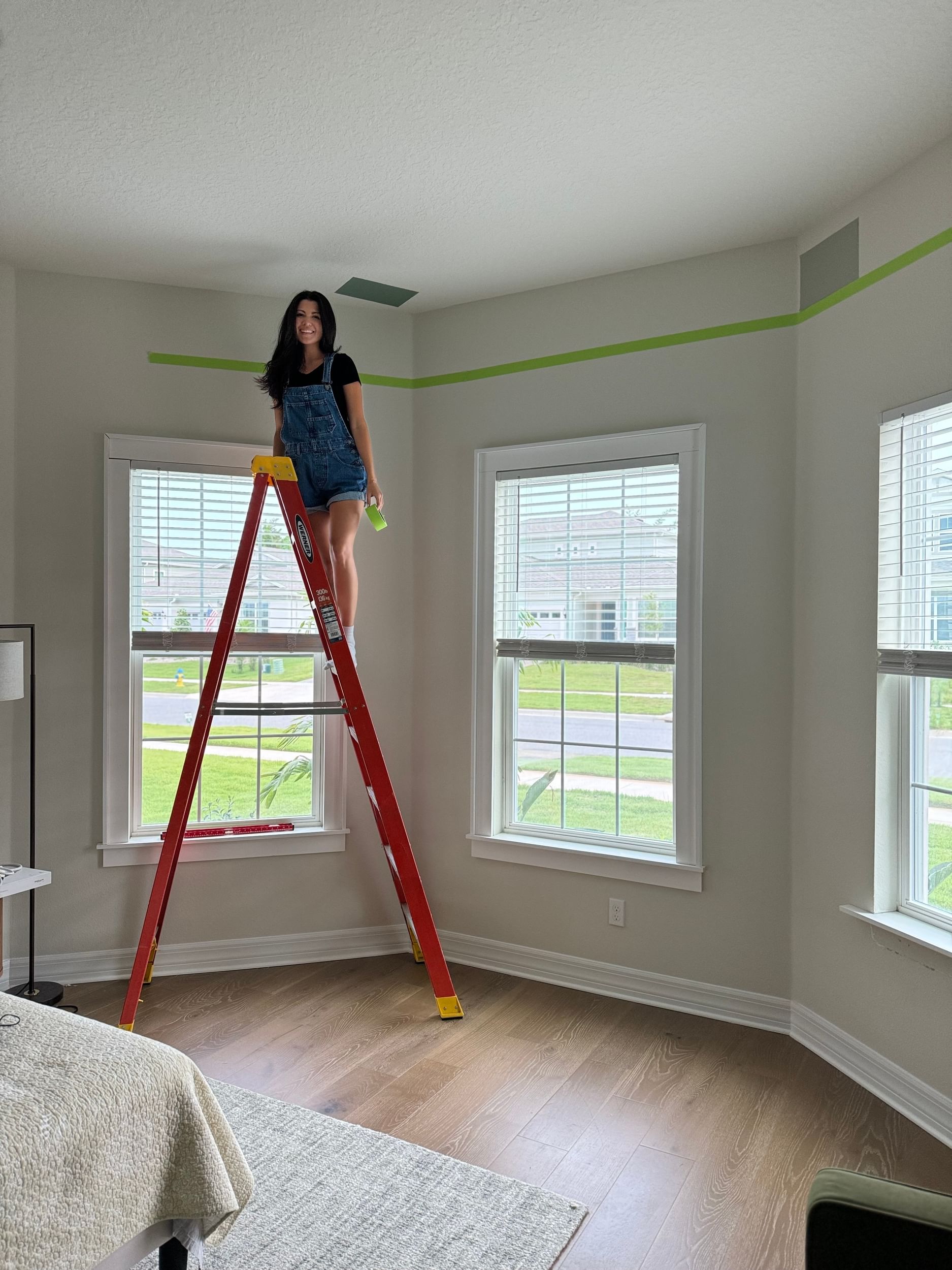 A woman on a ladder holding a roll of FrogTape Advanced