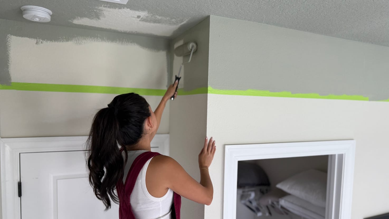 A woman painting her ceiling gray with a paint roller