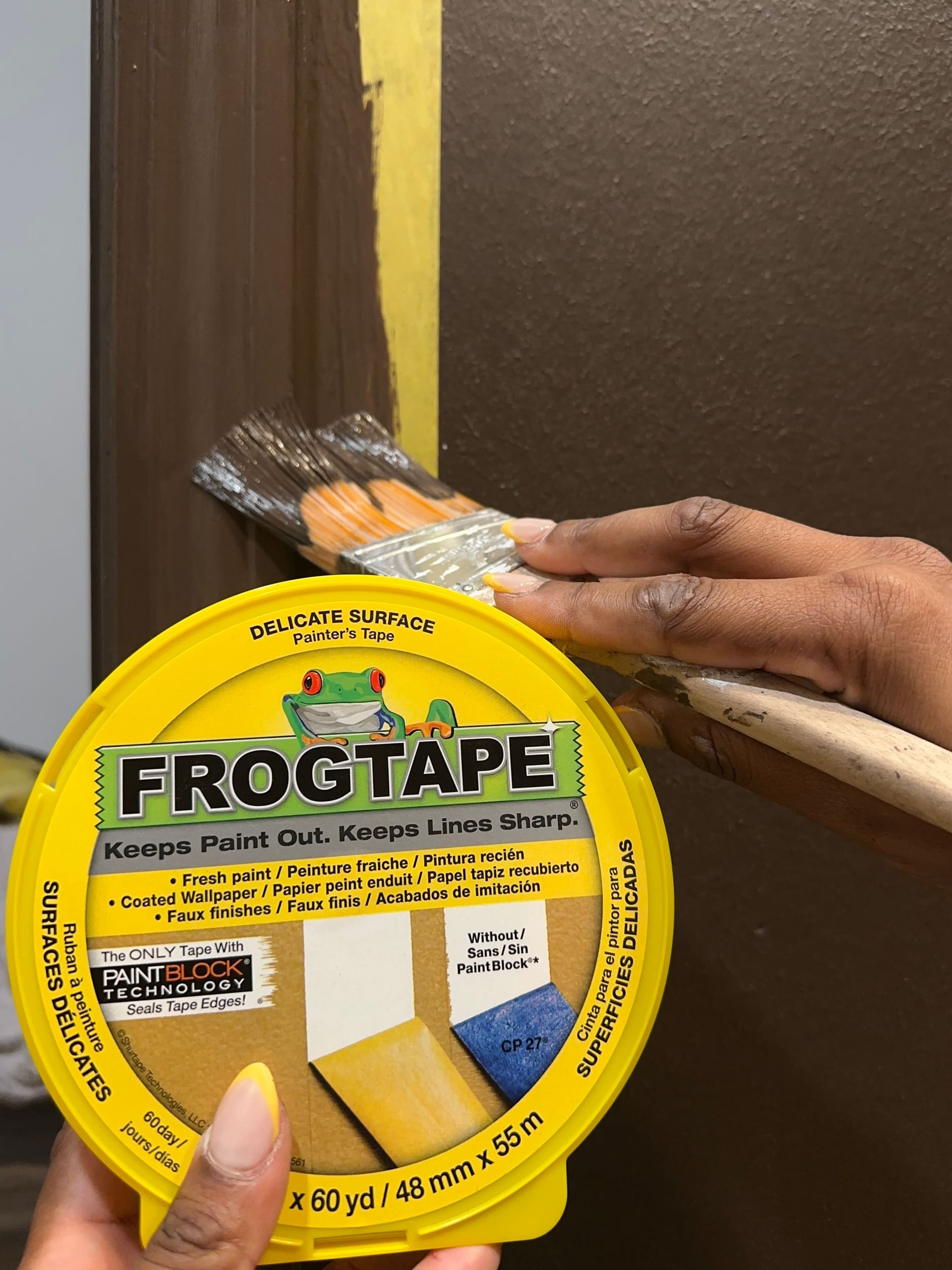 Yellow FrogTape Delicate Surface Painter's Tape Canister and Brown paint being painted on the wall behind it