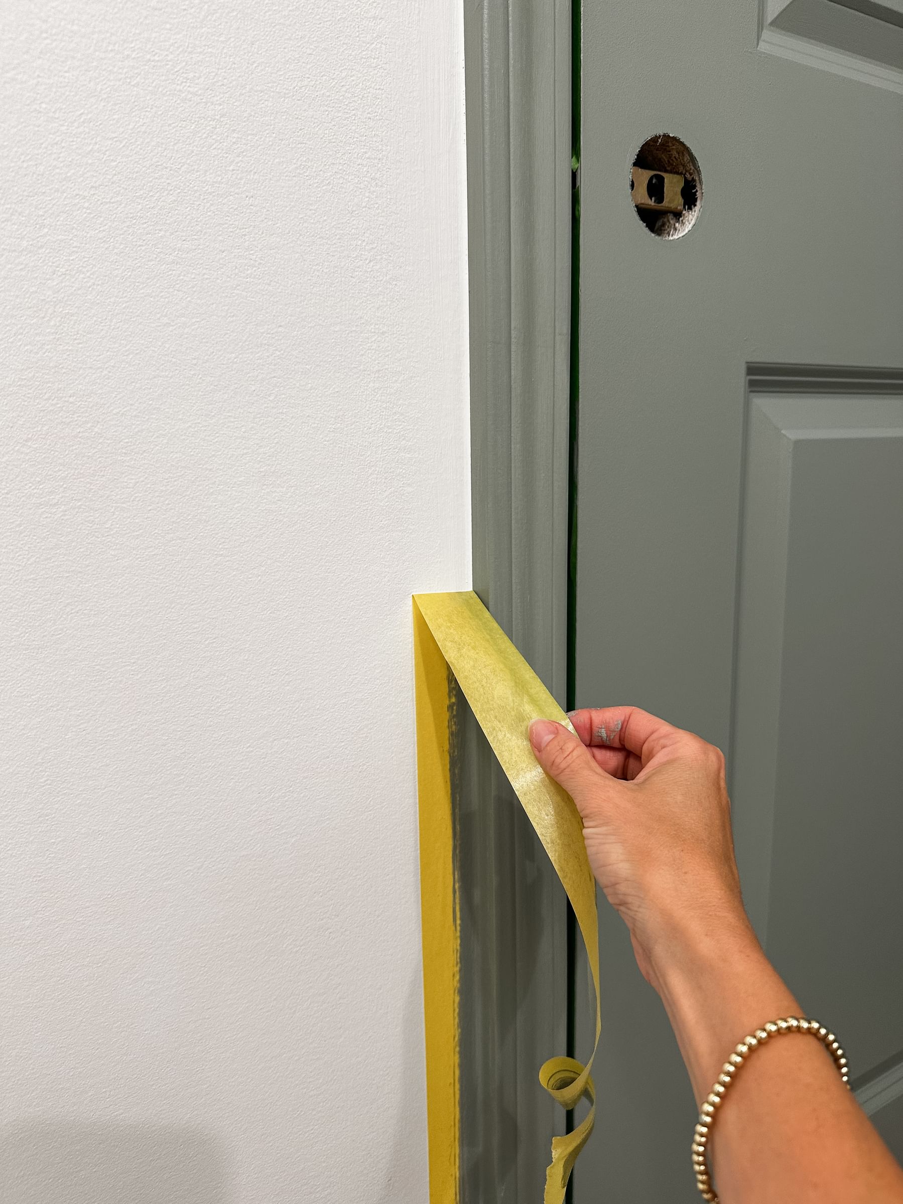 Tori Winkle Pulling off a piece of Yellow FrogTape Delicate Surface Painter's Tape from the wall to reveal a crisp line between the door trim and wall