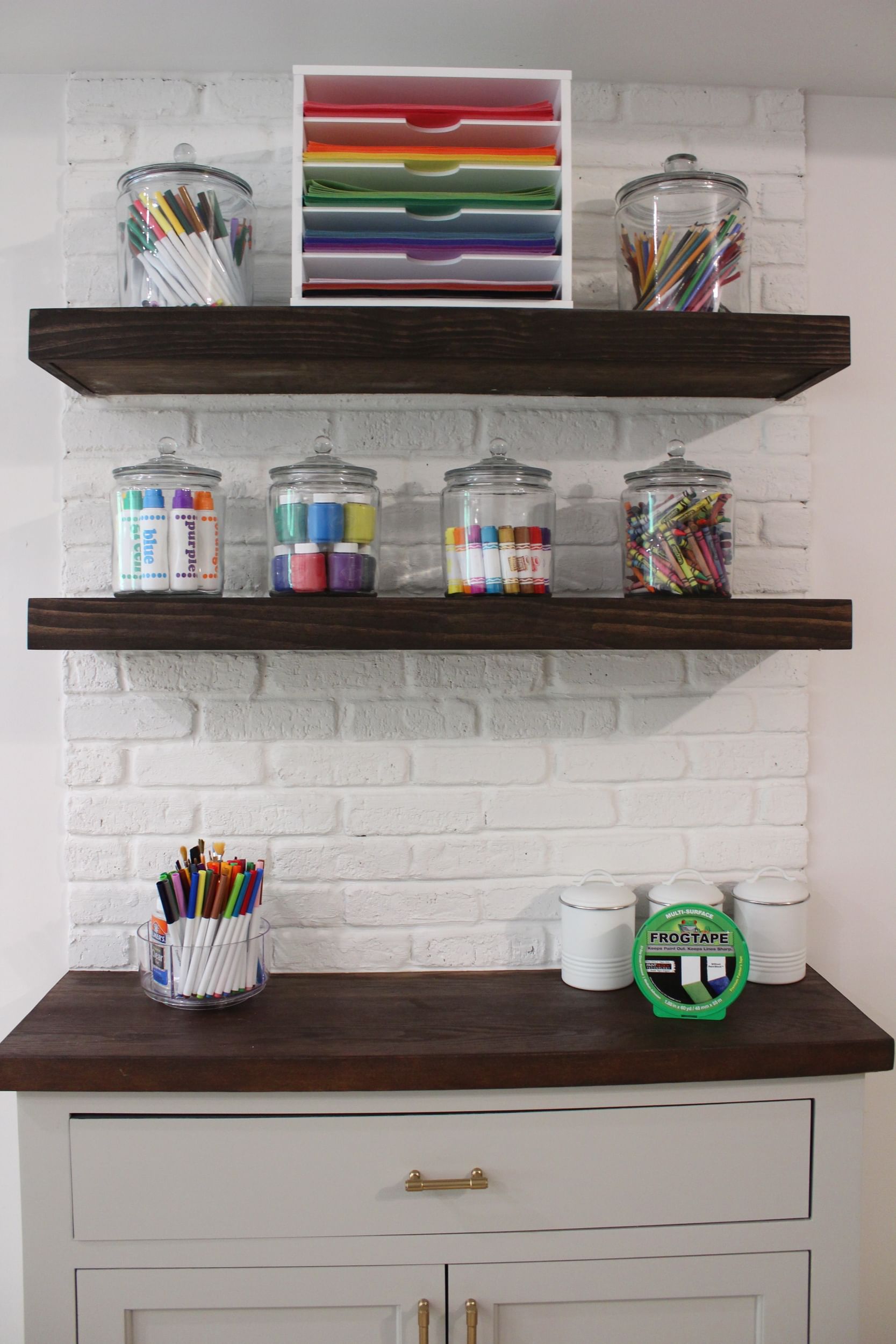 Coloring supplies organized on floating shelves and cabinet countertop with brick backsplash