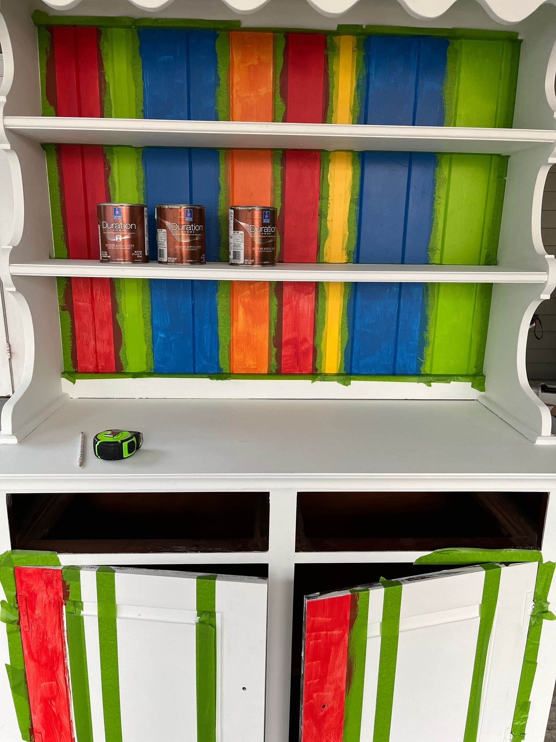 Red, green, blue, orange, and yellow painted hutch. the bottom doors are taped off with green FrogTape Multi-Surface Painter's Tape.