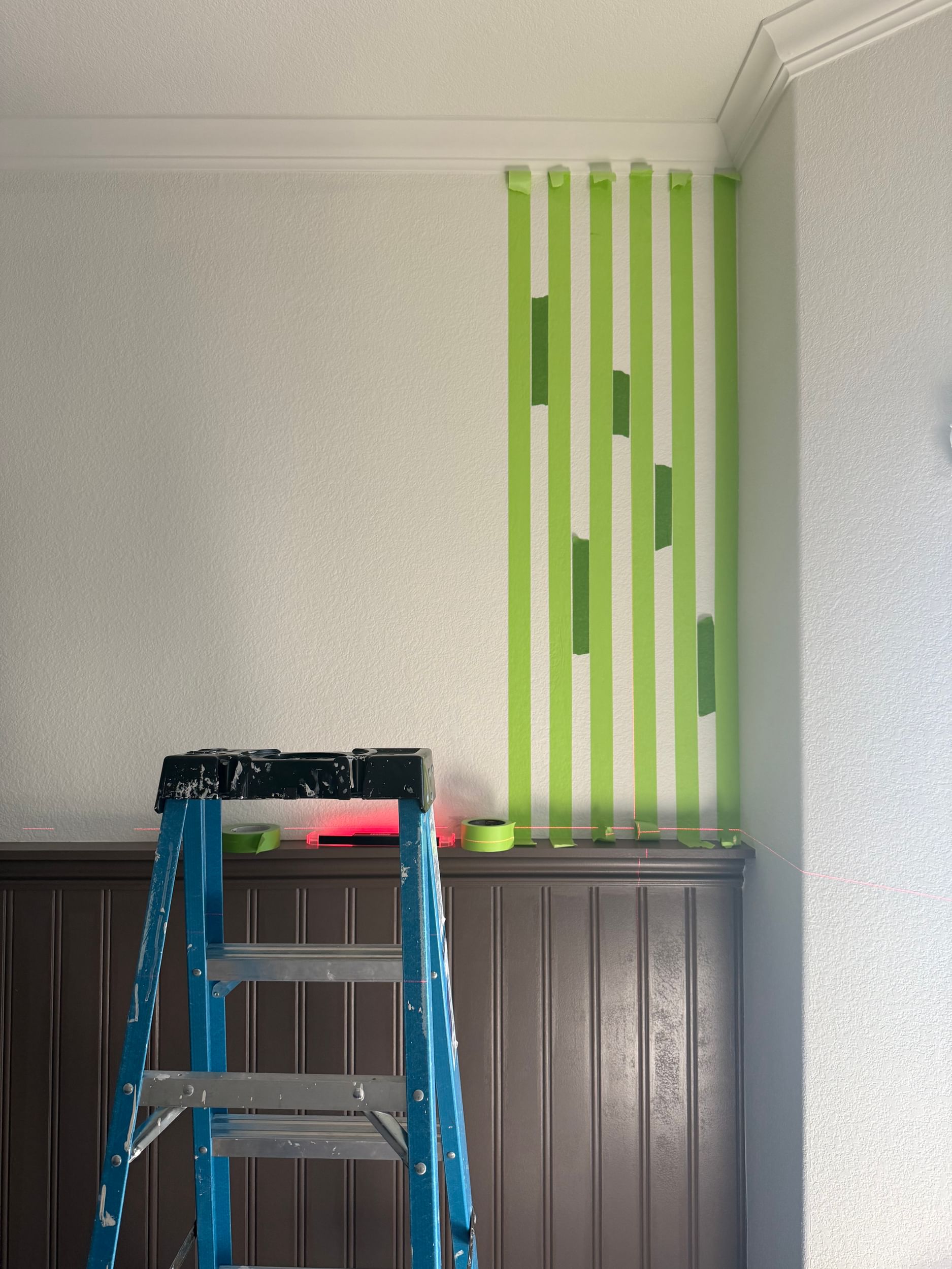 Vertical Stips of FrogTape Advanced on the right side of a white wall. There is a ladder and brown wainscotting