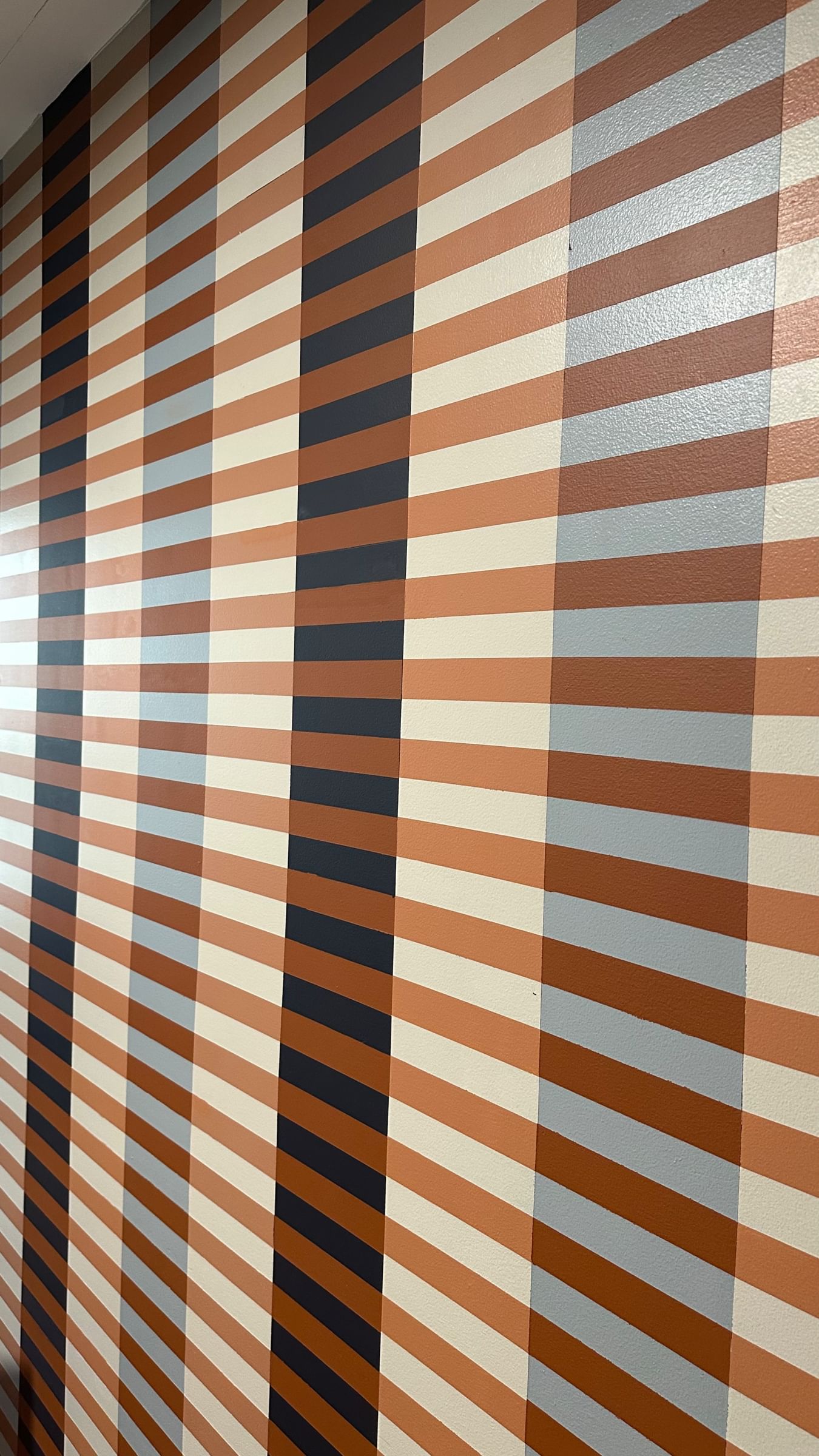 Striped pattern wall with vertical brown, cream, and dark blue bands intersected by horizontal lines, creating a retro, geometric aesthetic.