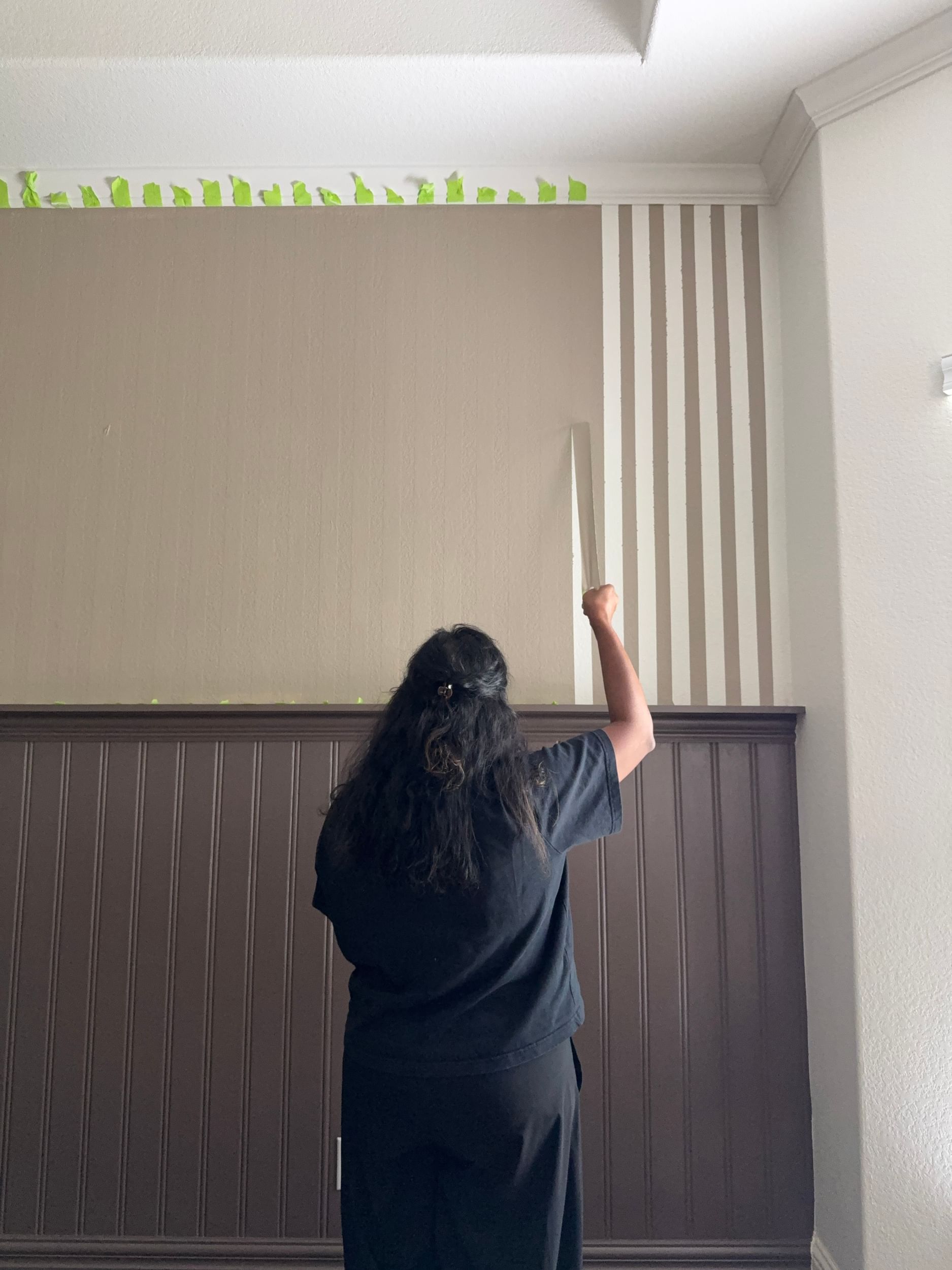 Vertical strips of FrogTape Advanced being peeled off of a wall to reveal crisp white and brown paint lines