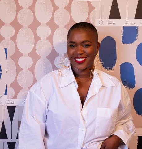 Smiling person in a white shirt and jeans poses confidently against a backdrop of abstract patterned wallpapers, creating a vibrant, joyful atmosphere.