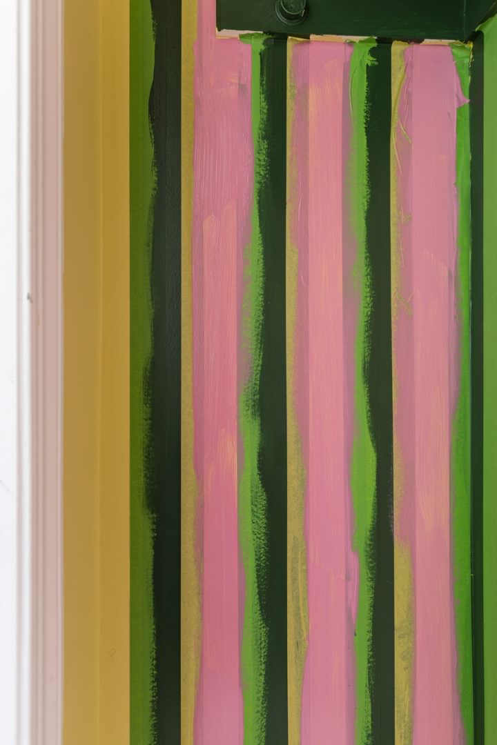 Yellow FrogTape Delicate Surface Painter's Tape lined vertically on a wall. The wall is painted with dark green and pink paint