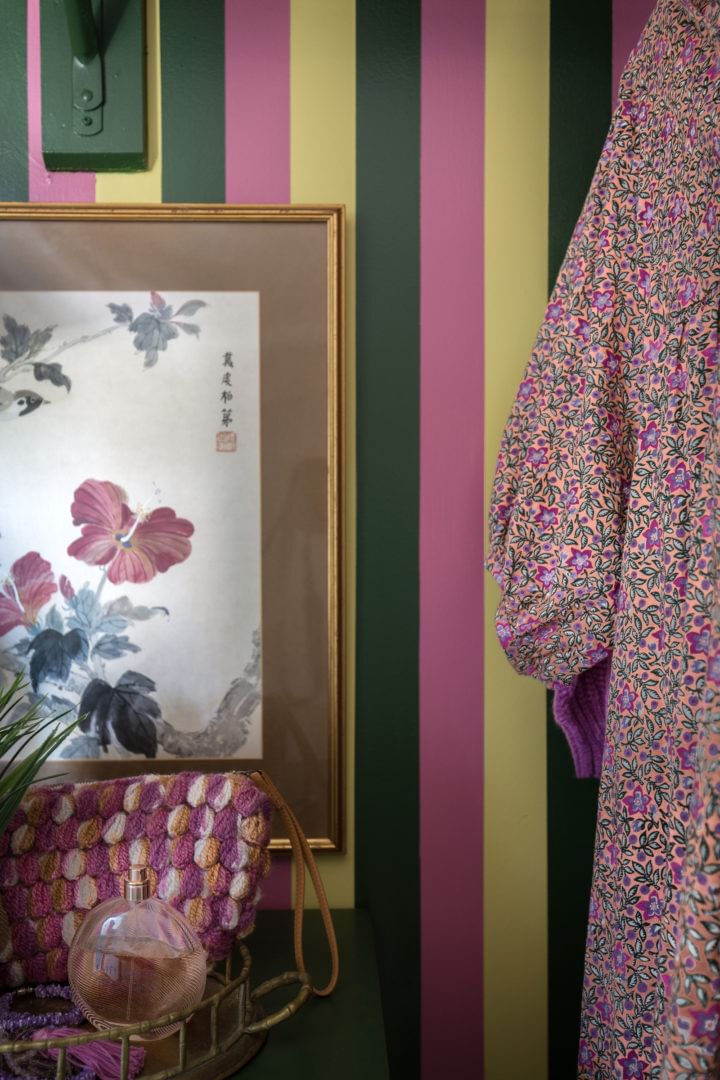 Green, Pink, and Yellow Striped wall with a Frame with a flower print and clothes hanging