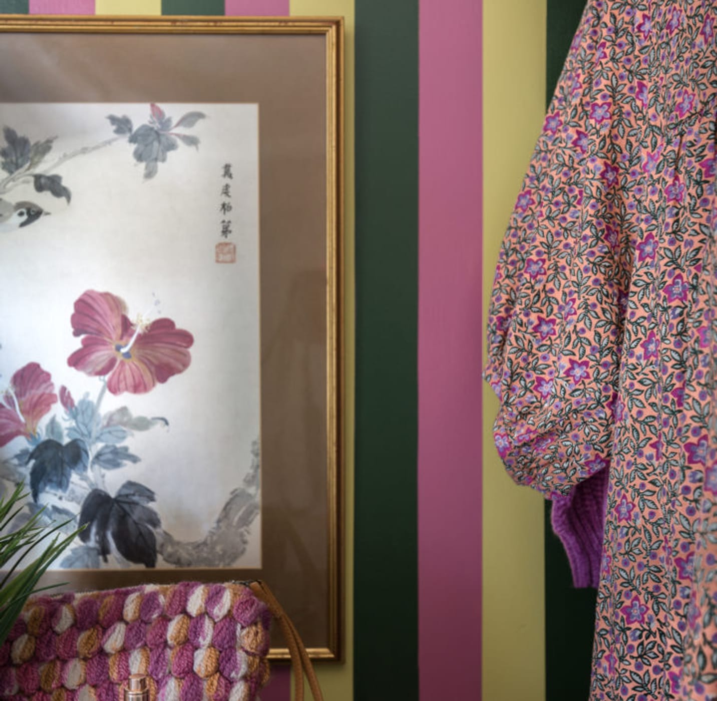 Green, Pink, and Yellow Striped wall with a Frame with a flower print and clothes hanging