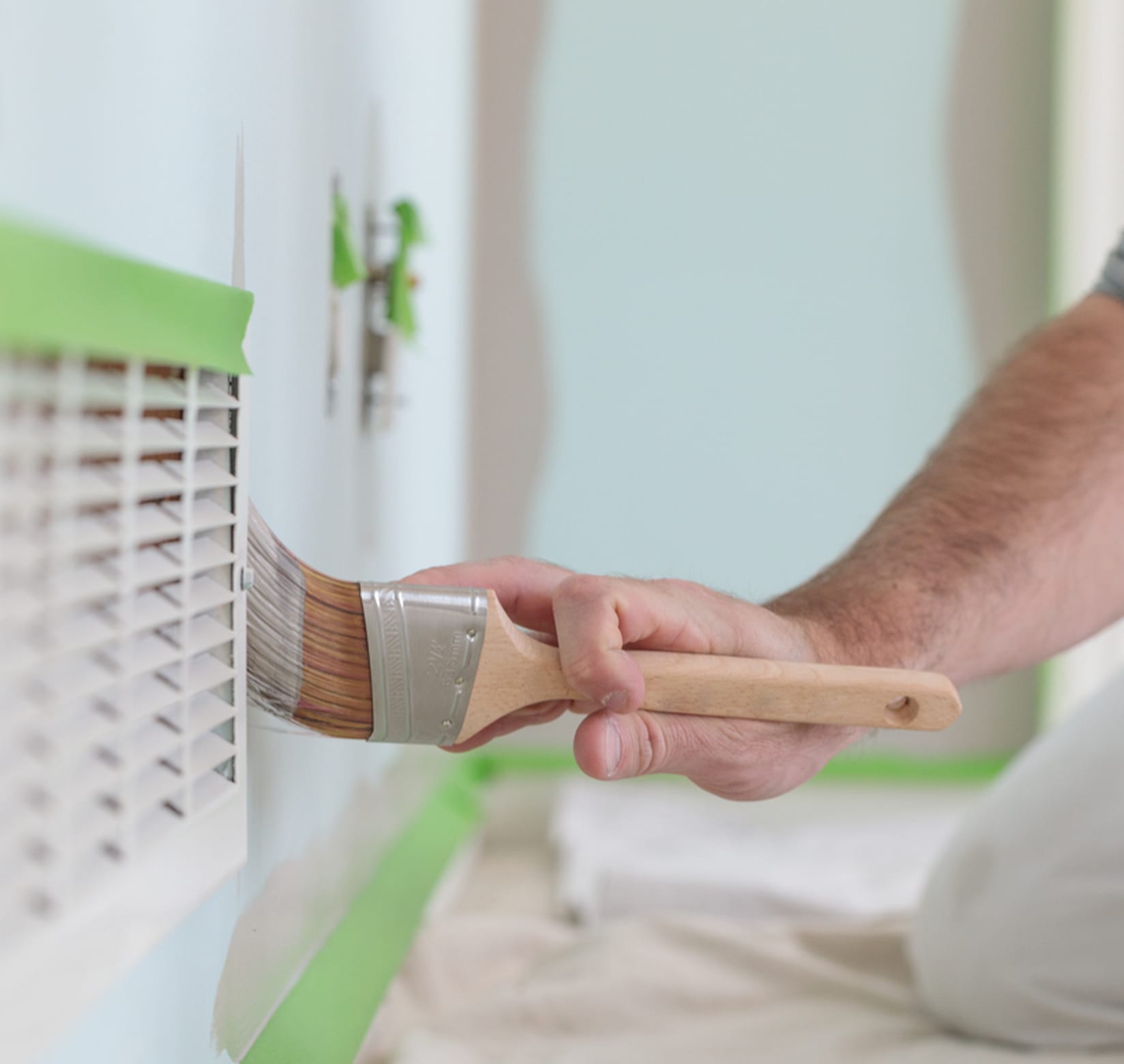 A man painting a blue wall gray. The trim is taped off with Green FrogTape Multi-Surface Painter's Tape