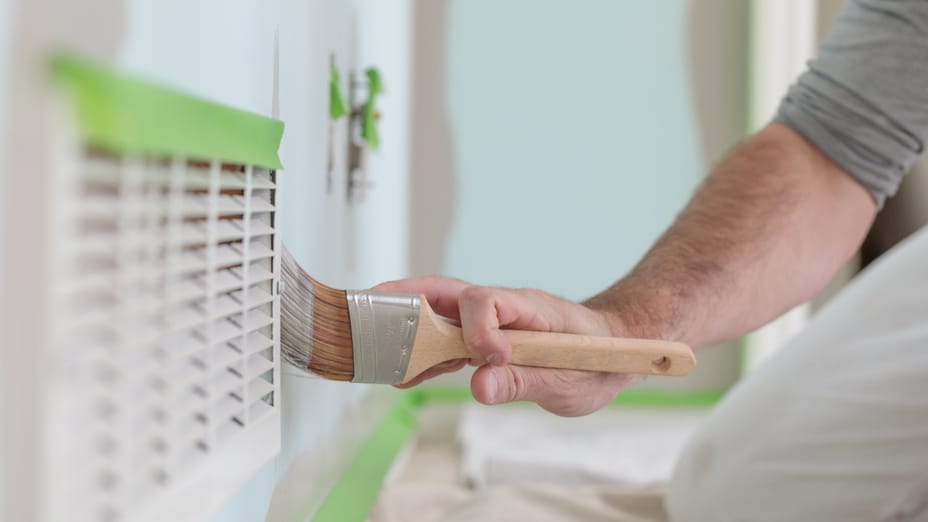 A man painting a blue wall gray. The trim is taped off with Green FrogTape Multi-Surface Painter's Tape