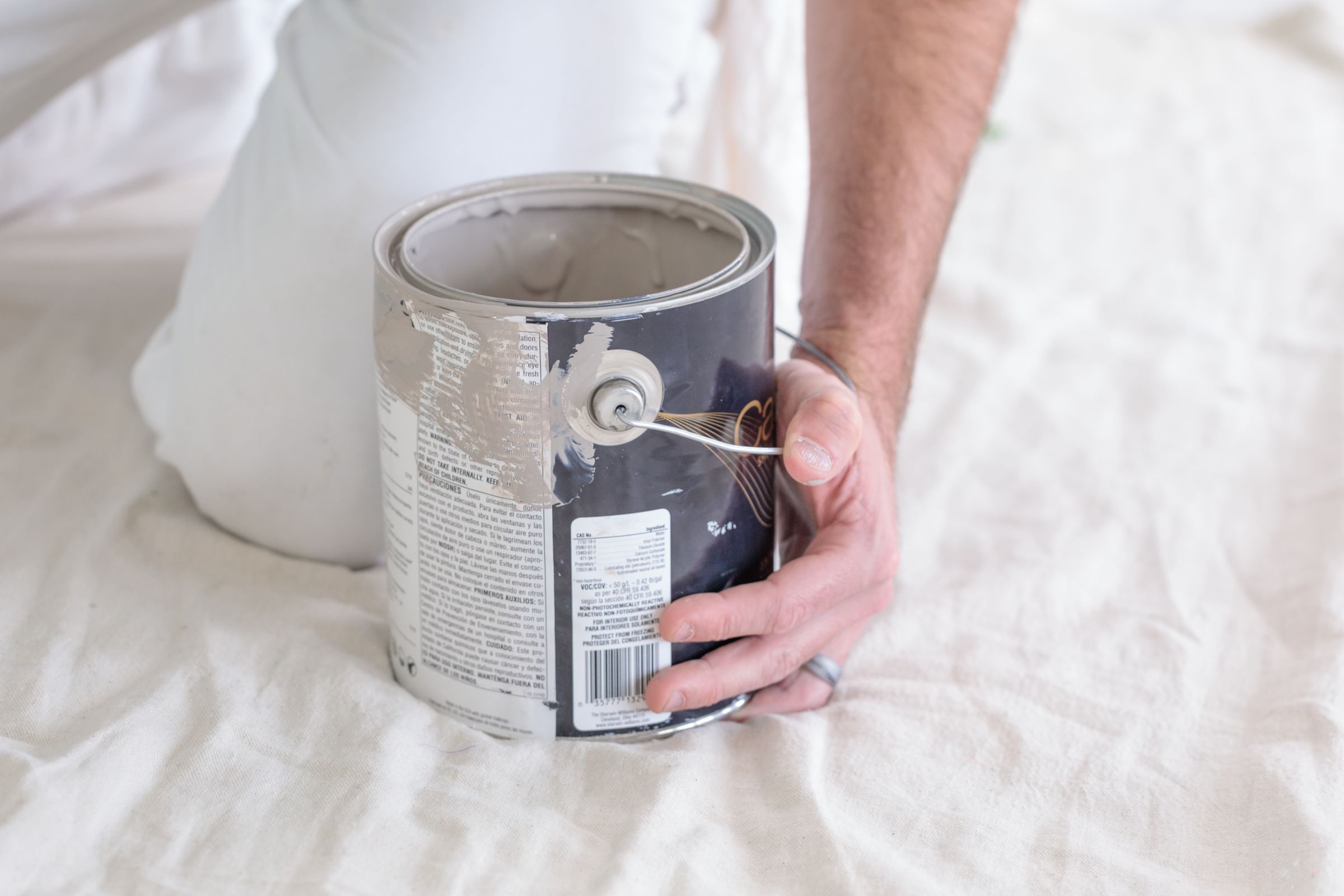A Painter stabilizing an Open Paint Can on a Drop Cloth with one hand
