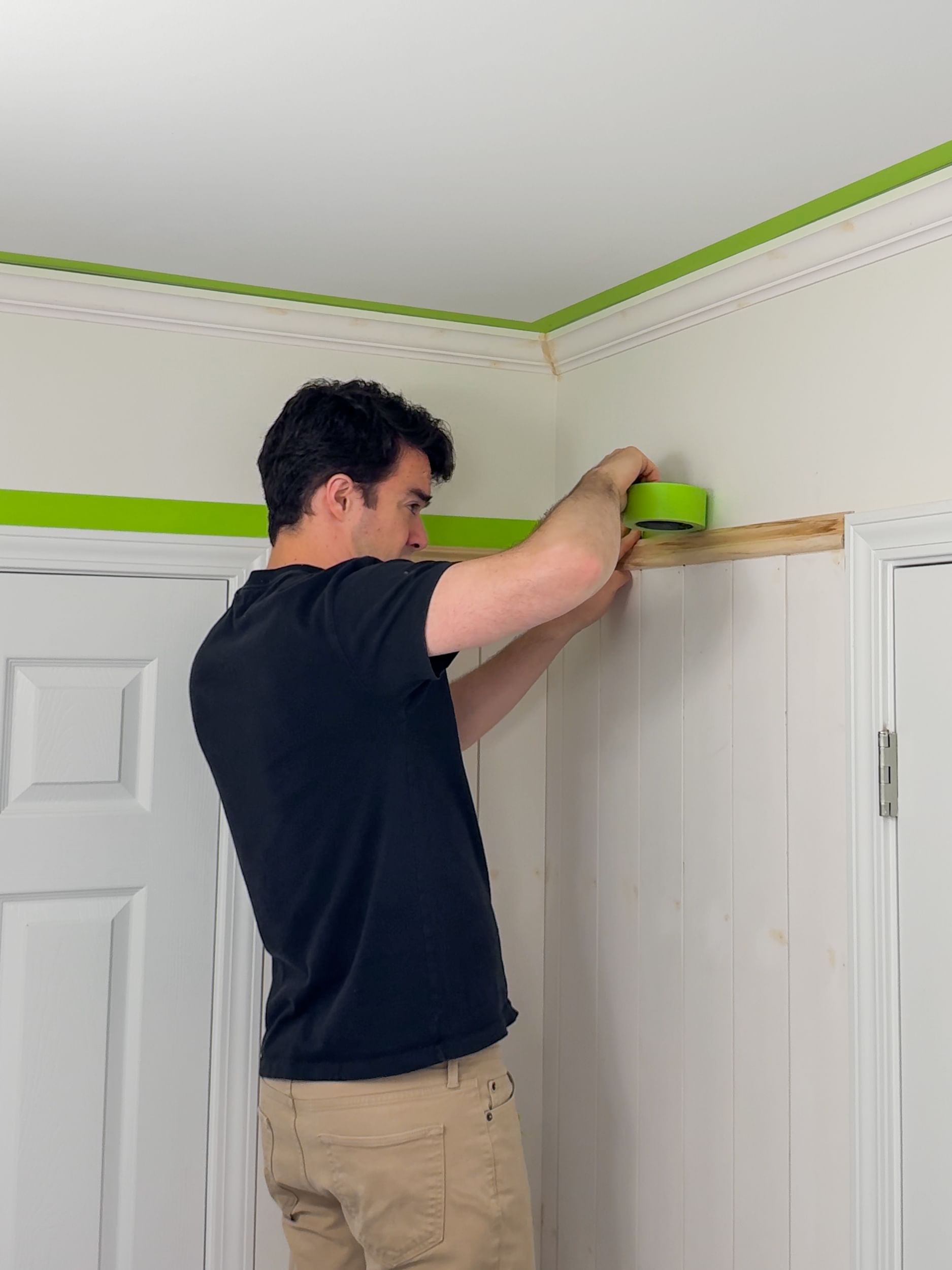 A man applying FrogTape Advanced Painter's Tape to a wall where the upper door trim meets the wall