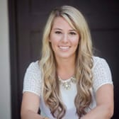 A woman with long, wavy blonde hair and a white lace top smiles warmly at the camera, creating a friendly and welcoming atmosphere.