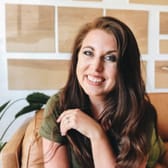 Smiling woman with long brown hair sitting on a tan sofa, wearing a green shirt. Abstract art decor in the background sets a warm, inviting tone.