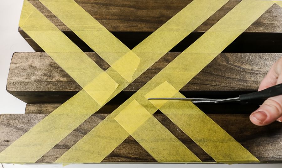 Wooden Shelves with yellow FrogTape Delicate Surface Painter's Tape taped across and a hand with scissors cutting the tape.
