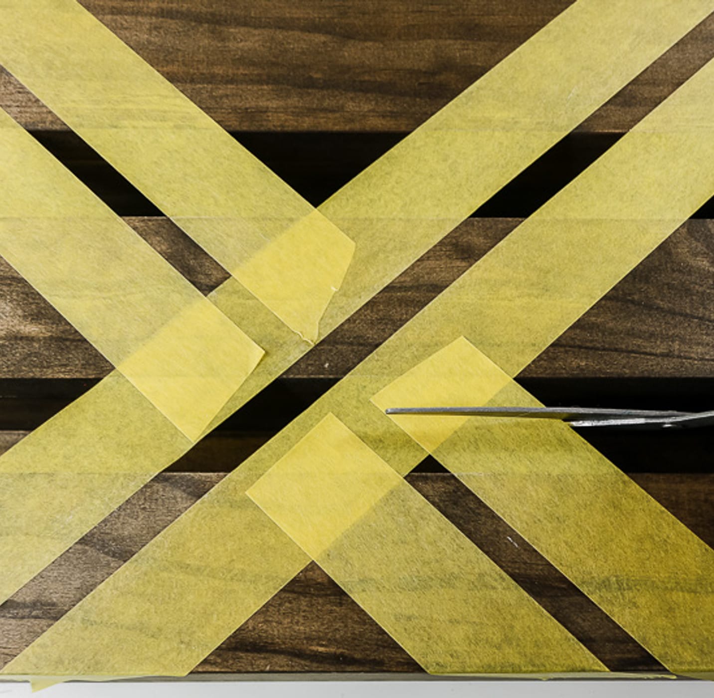 Wooden Shelves with yellow FrogTape Delicate Surface Painter's Tape taped across and a hand with scissors cutting the tape.