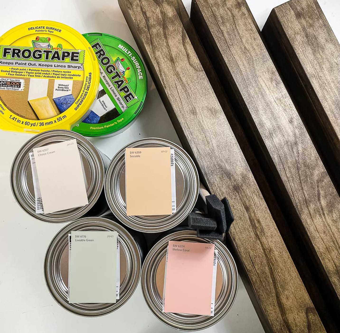 Wooden Shelves with paint cans with swatches on the lips. There is also a container of FrogTape Delicate Surface Painter's Tape, and a container of FrogTape Multi-Surface Painter's Tape.