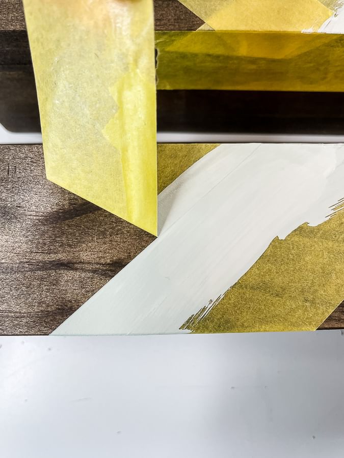 Yellow FrogTape Delicate Surface Painter's Tape being peeled off of a wooden shelf to reveal a crisp white paint line.