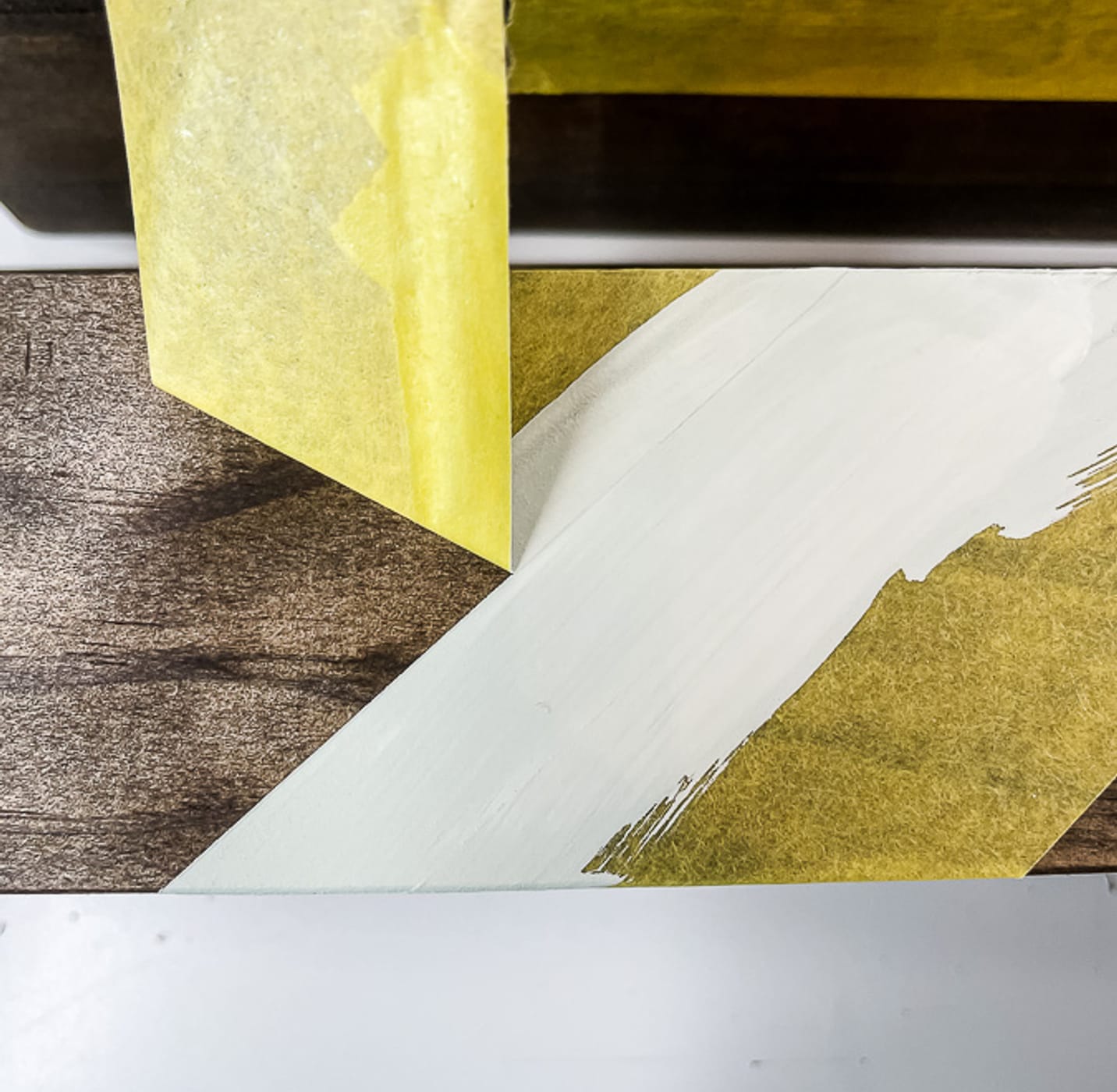 Yellow FrogTape Delicate Surface Painter's Tape being peeled off of a wooden shelf to reveal a crisp white paint line.