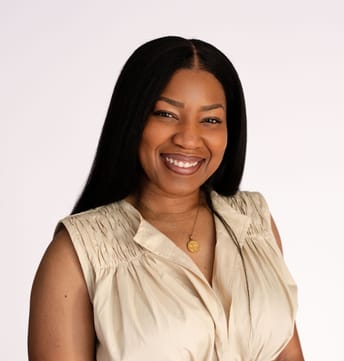 Smiling woman with long dark hair wearing a beige sleeveless blouse and a necklace, set against a plain white background. The tone is warm and friendly.