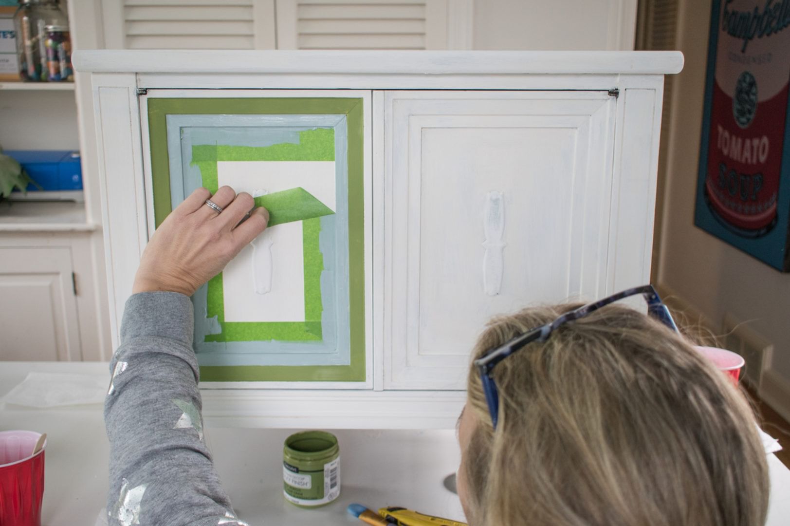 Green FrogTape Multi-Surface Painter's Tape being peeled off of the door of a small white end table