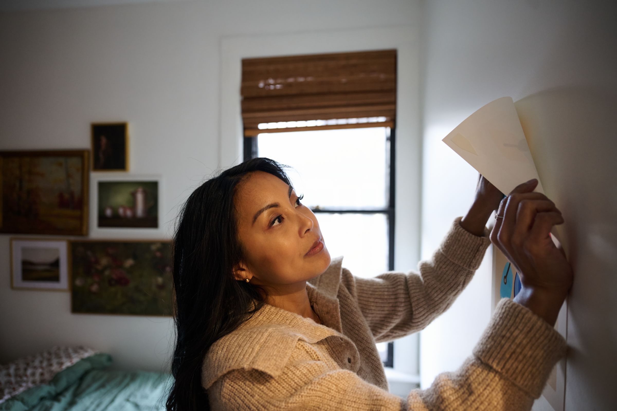 Woman hanging a poster on the wall using FrogTape reMOVEables Poster Strips