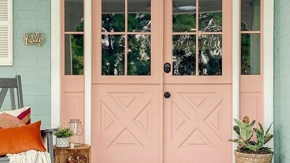 Front Porch with Pink Front Door with big windows, white trim, and teal siding. There is a rocking chair with some pillows and a blanket, and a potted plant.