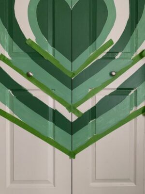 A green Heart Mural on a white closet door. The bottom points of the hearts are taped off in a V shape with Green FrogTape Multi-Surface Painter's Tape