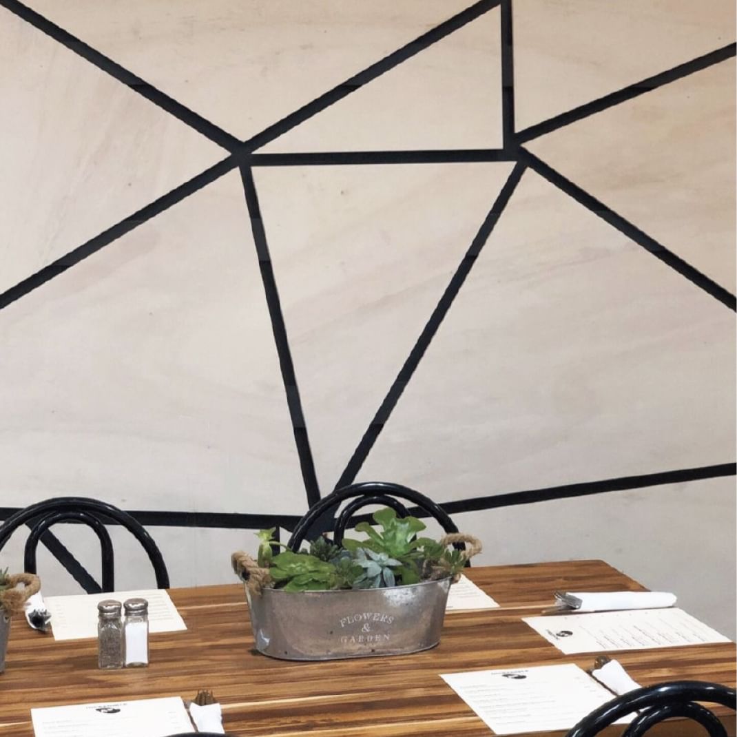 Triangular geometric black lined pattern on a white wall. Below is a small wooden kitchen table with black chairs.