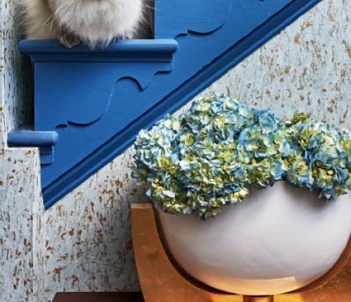 Close up of blue staircase, a side table with a large white pot with flowers.