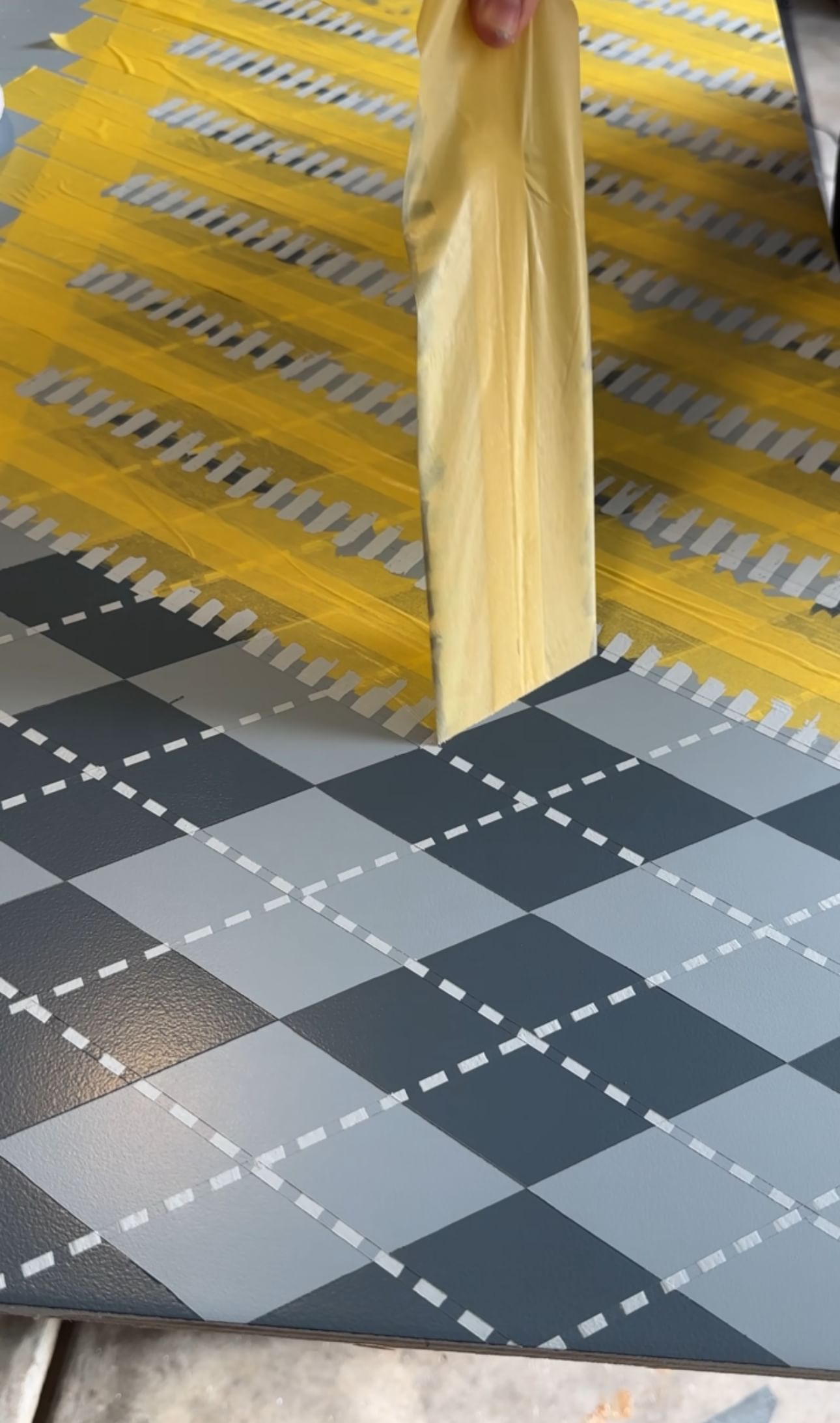 Yellow Delicate Surface Painter's Tape being peeled off of a piece of painted drywall to reveal an Argyle Pattern