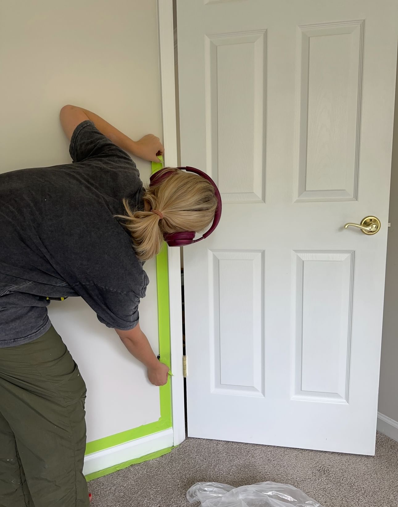 A woman applying FrogTape Advanced to where the door trim meets the wall in a room