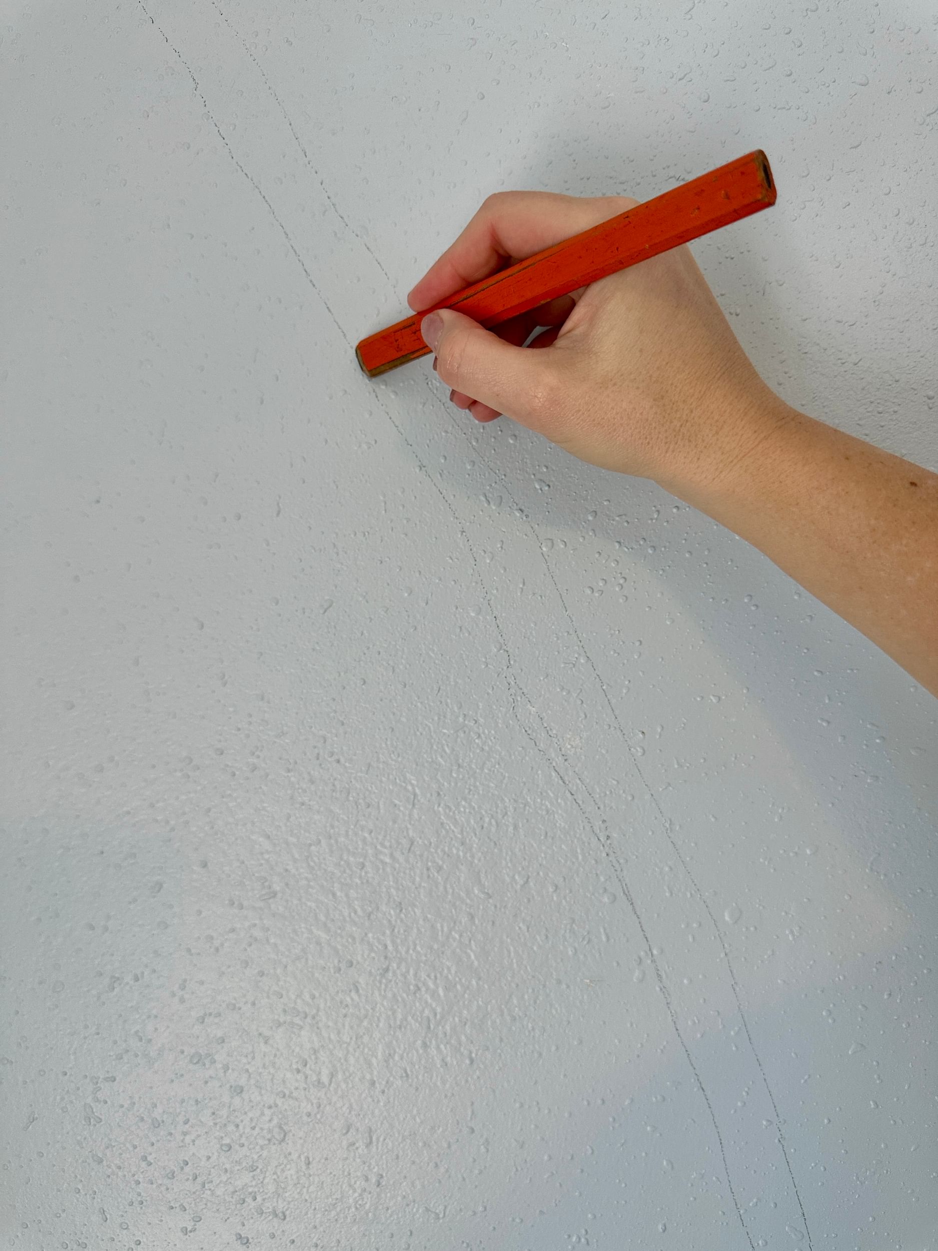 A hand using a red contractors pencil to sketch out lines on a wall
